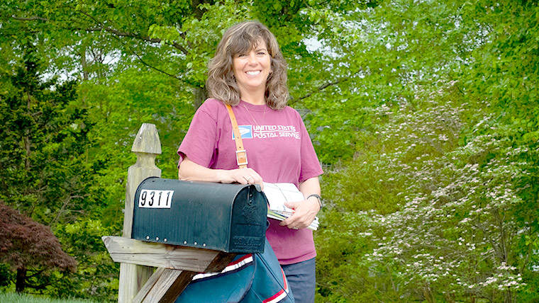 USPS Assistant Rural Carrier standing outside by a mailbox.