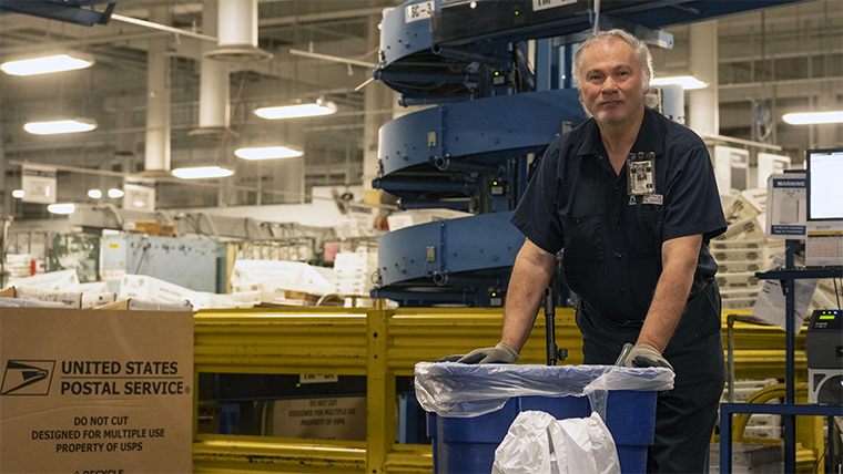 An USPS Laborer Custodial stands holding cleaning tool.