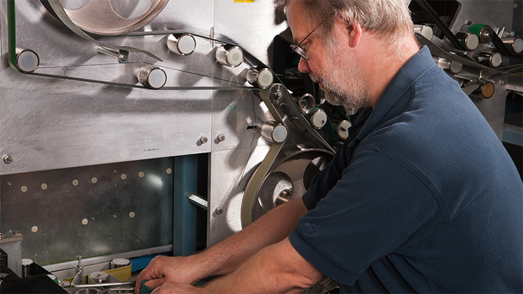 An USPS Maintenance Mechanic Mail Processing Equipment(MPE) standing front of machine, holding a tool.