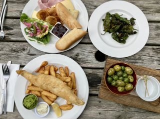 A table full of large plates of traditional pub grub like fish’n’chips and a ploughman’s, with smaller plates of olives and Padron peppers.