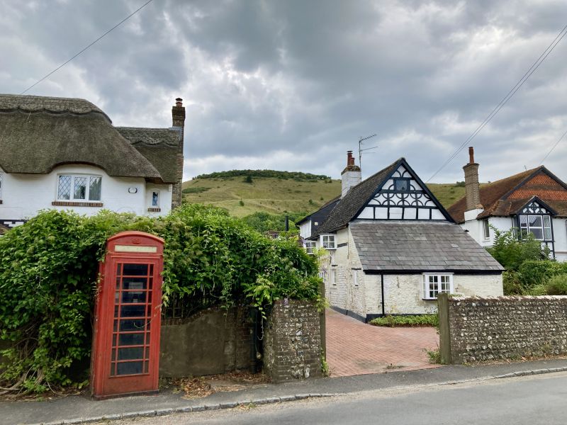 Quaint half-timbered houses with an old red telephone box in front of them and green hills behind.