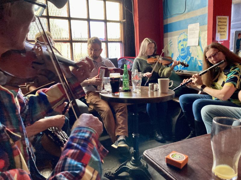 A group of fiddlers and box players playing in the corner of a pub.