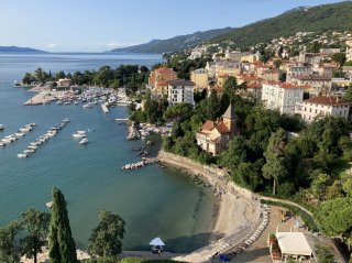 A beautiful old town interspersed with lush greenery sweeps down to a tranquil bay with blue/green water.