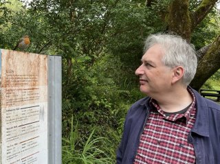 Me standing near a sign in the woods with a robin redbreast perched on it.