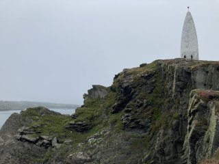 Tiny figures in the distance at the bottom of a tapered tower on a cliff top.