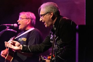 A profile shot of me on stage with my mandolin singing with one arm extended.