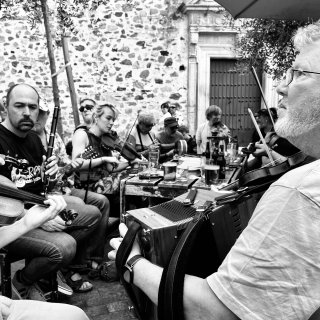 Loads of musicians playing around a table in a medieval courtyard.