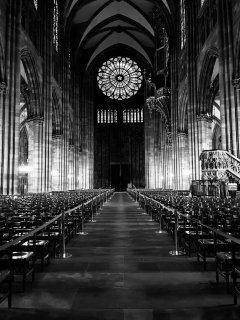 Looking down the aisle of a cathedral at a magnificent rose window flanked by towering columns.