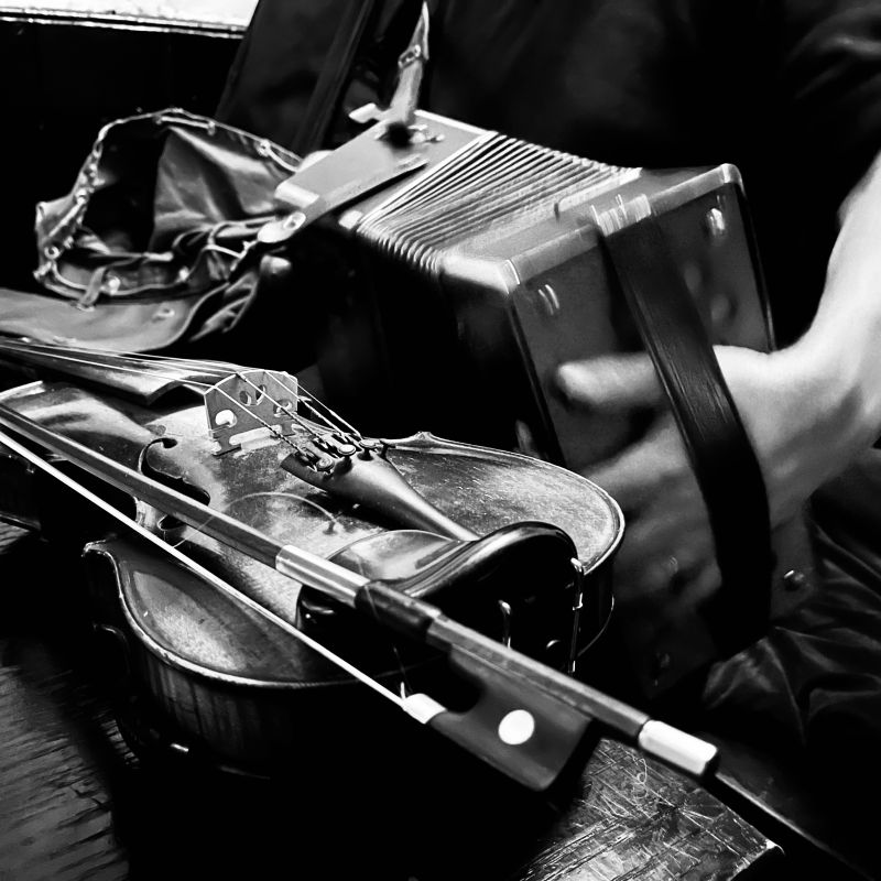 Close up of a fiddle lying on a table in front of an accordion being played.