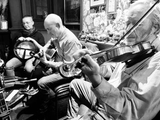 A fiddlers, guitar player and bodhrán player all in a row.