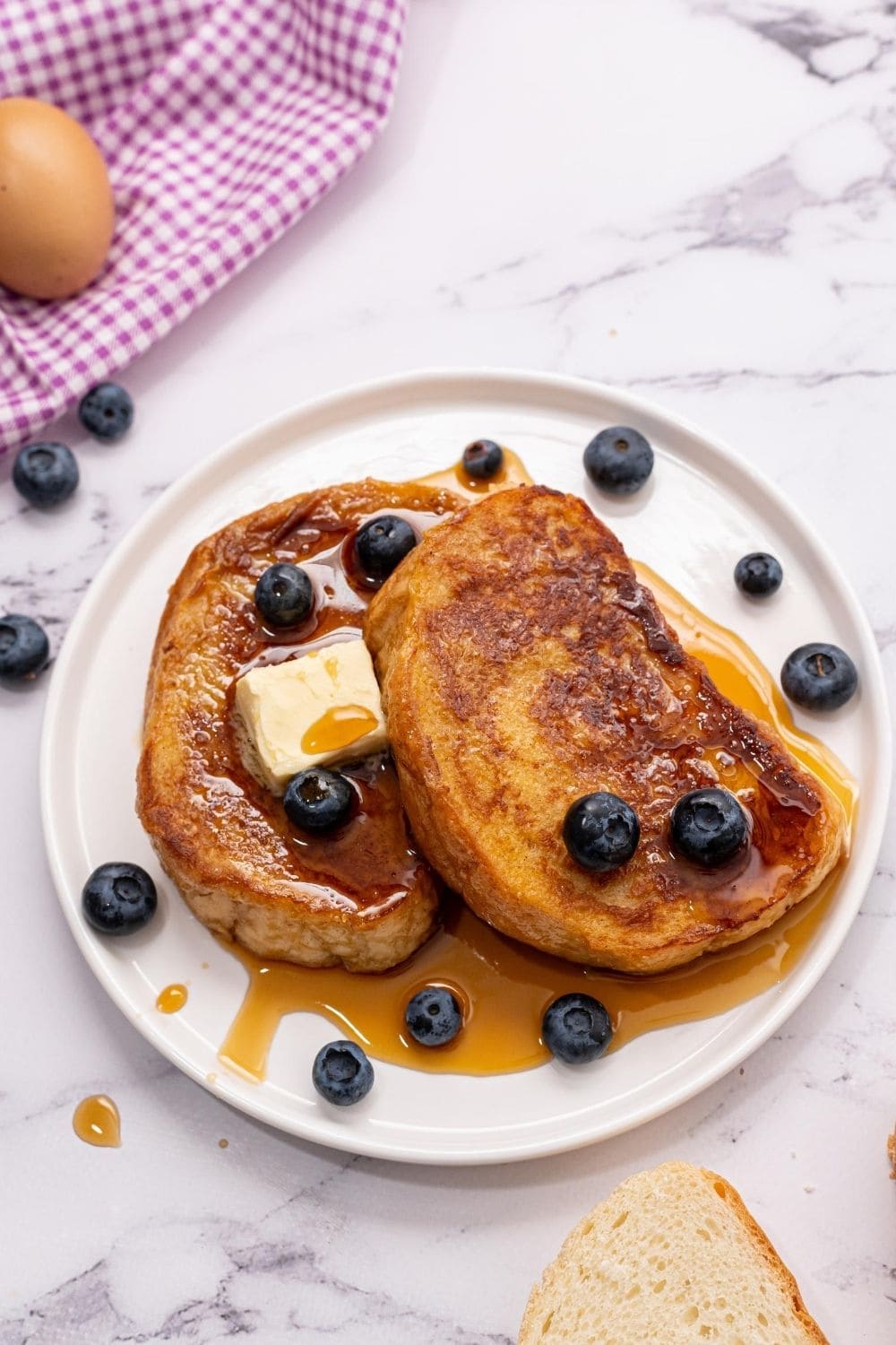 2 slices of french toast on white plate topped with maple syrup and blueberries