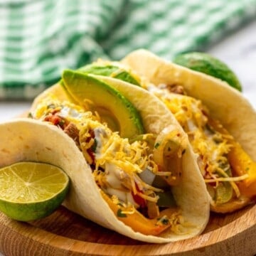 Two assembled steak fajitas on wooden plate served with sliced avocado.