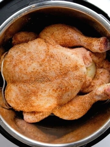 Whole seasoned chicken on trivet inside inner pot.