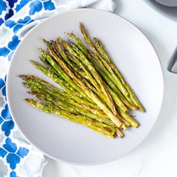 A plate of crispy asparagus next to air fryer.