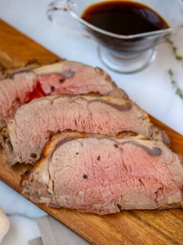 Sliced new york strip roast on cutting board with aus jus in background.