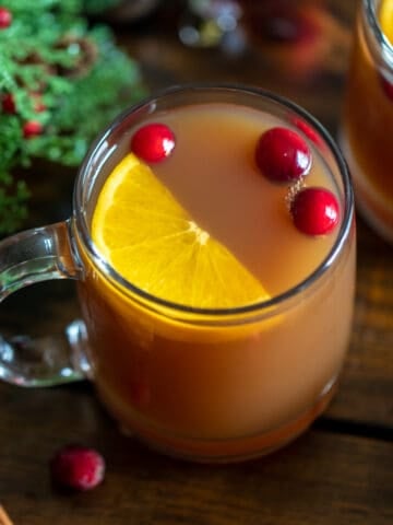 Top down view of glass of spiced Christmas tea served with wedge of an orange and fresh cranberries.