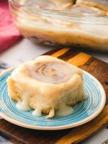 Healthy Cinnamon Roll on blue serving plate with tray of cinnamon rolls in background.