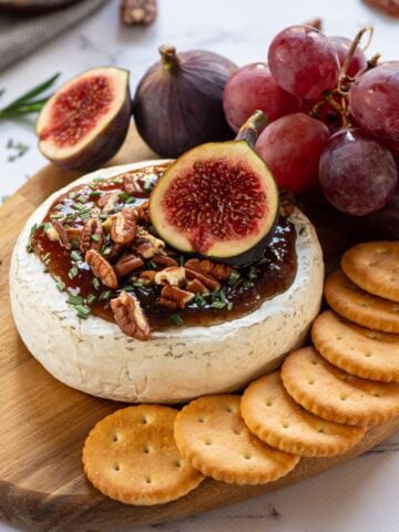 Baked Brie on cutting board topped with fig jam, walnuts, and fresh figs.