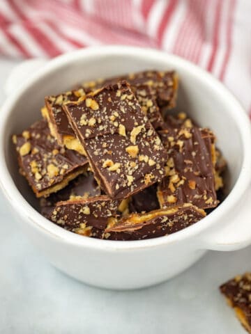 Bowl of saltine cracker toffee with walnuts and chocolate chips on counter.