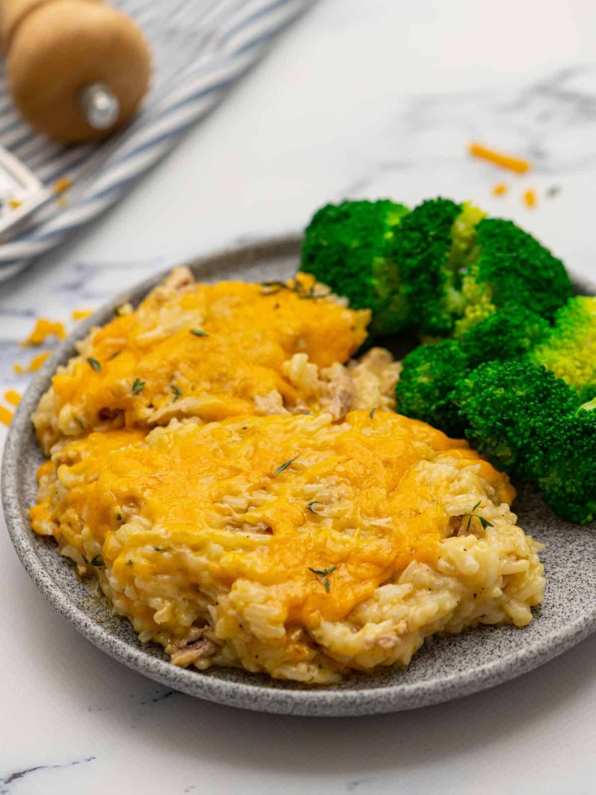 Plated cheesy chicken and rice casserole on plate next to steamed broccoli.