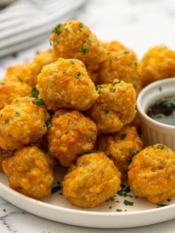 Plate of homemade sausage balls with cheese served next to a bowl of maple syrup.