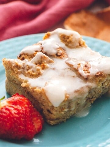 A piece of Overnight French Toast Casserole on blue plate with strawberries on side.