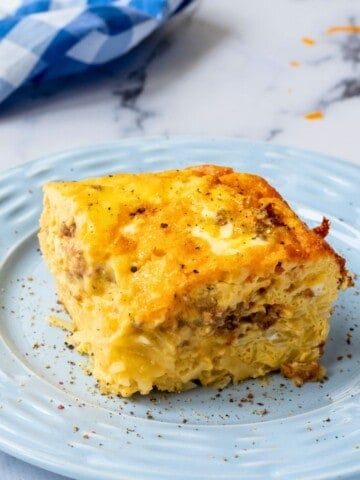 A slice of hashbrown breakfast casserole made with sausage and cheese on white plate.