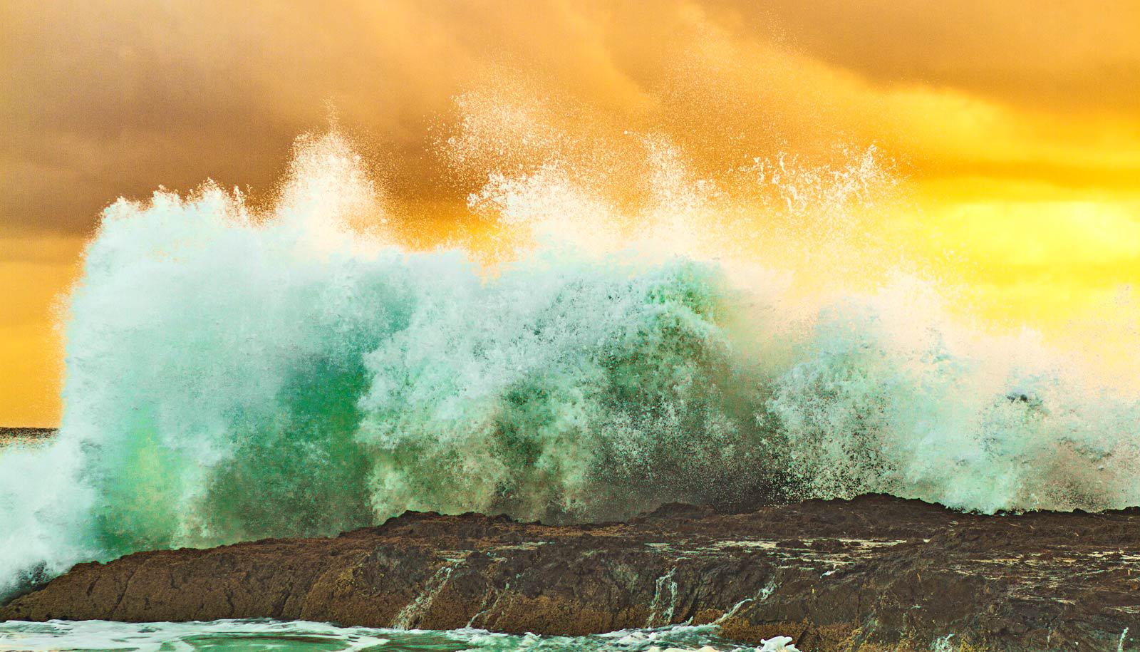 wave crashes against rocks at sunset