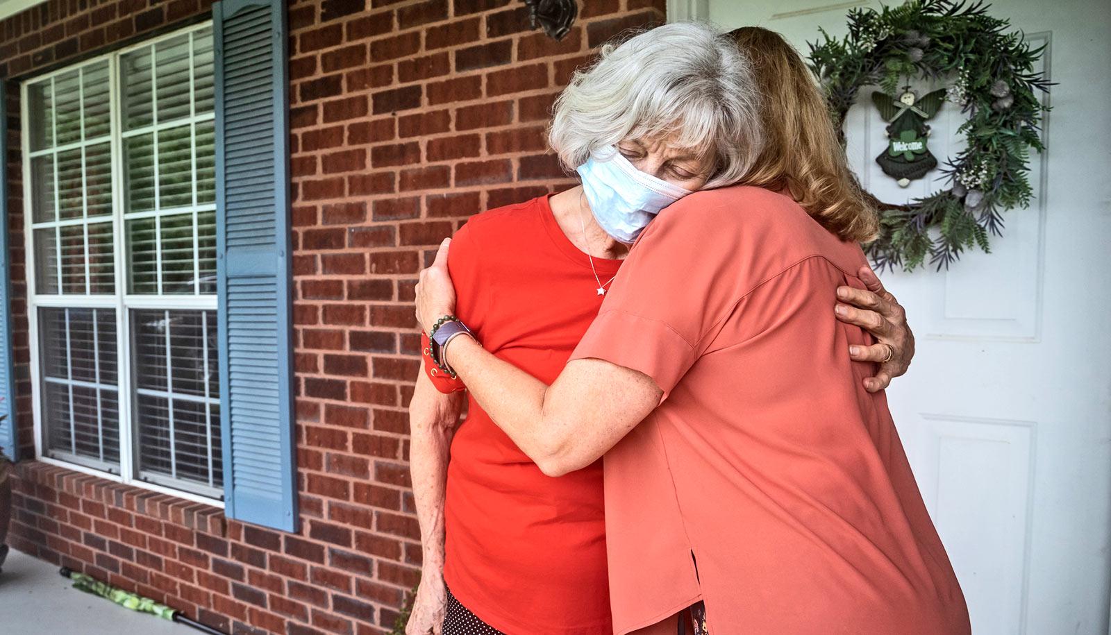 adult hugs elderly person on front porch