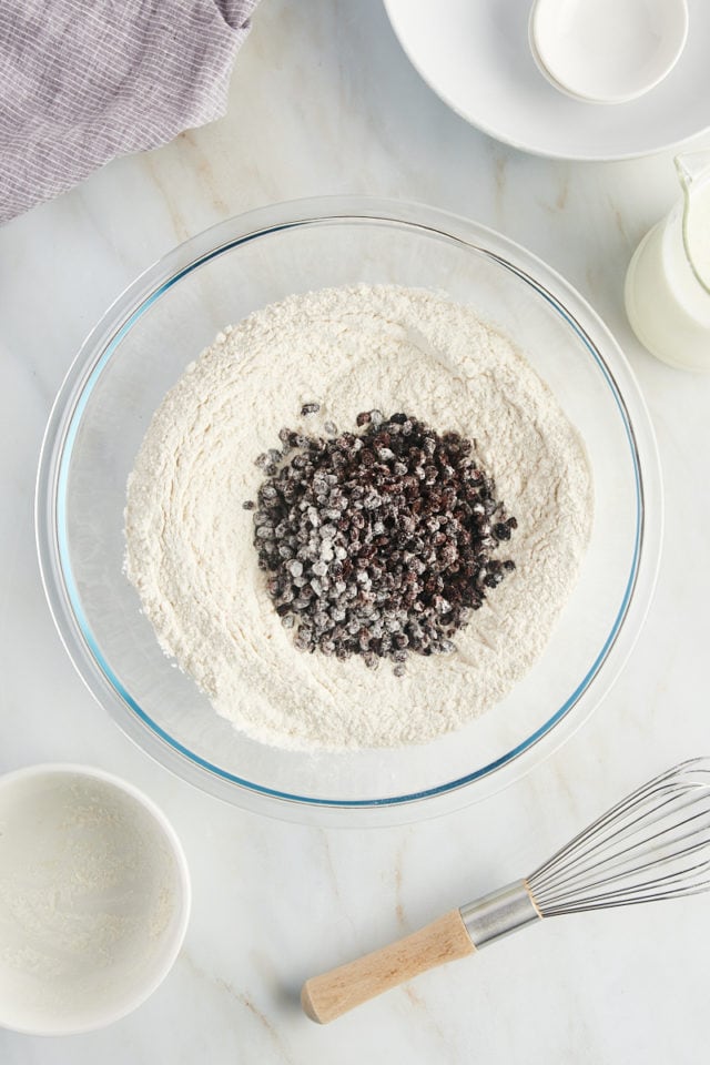 overhead view of dried currants added to dry ingredients in a glass mixing bowl