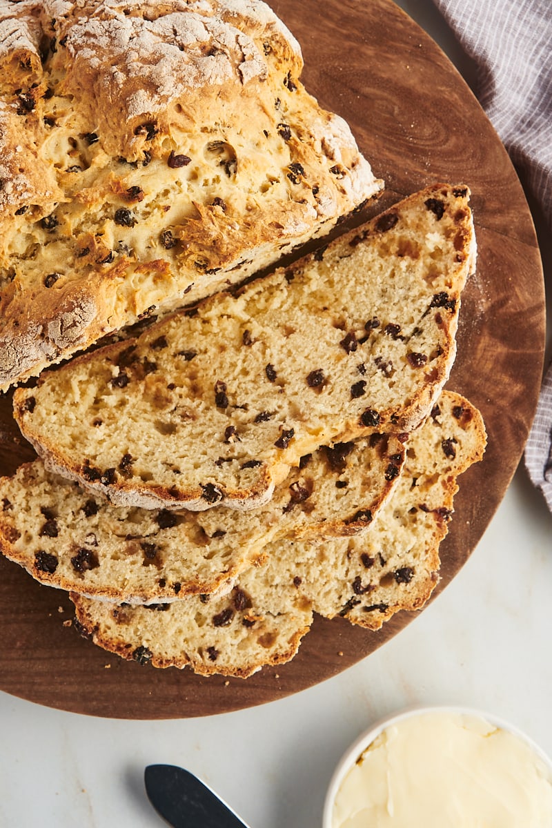 overhead view of partially sliced Irish soda bread on a wooden board with a small bowl of butter beside