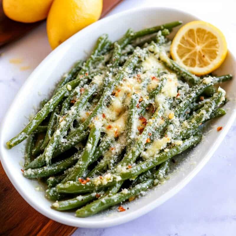 This image shows a delicious dish of roasted green beans topped with Parmesan cheese and red pepper flakes, garnished with slices of lemon. This looks like a great option for a Keto Thanksgiving Side — easy to prepare, flavorful, and low in carbs, perfect for a holiday spread!