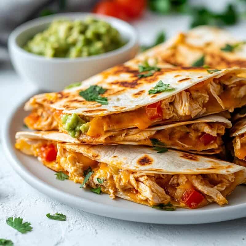 Golden and crispy Chicken Quesadillas stacked on a plate, served with guacamole, ideal for Cinco de Mayo celebrations.