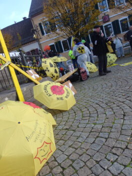 Regenschirme mit Antiatom Sonne, Gelbes Widerstands X und eine Person spricht ins Mikrofon.