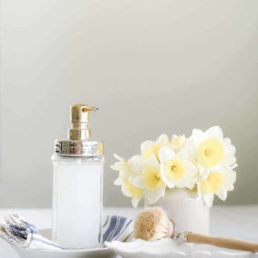 Liquid hand soap in glass jar pictured with daffodils and wooden scrubbing brush