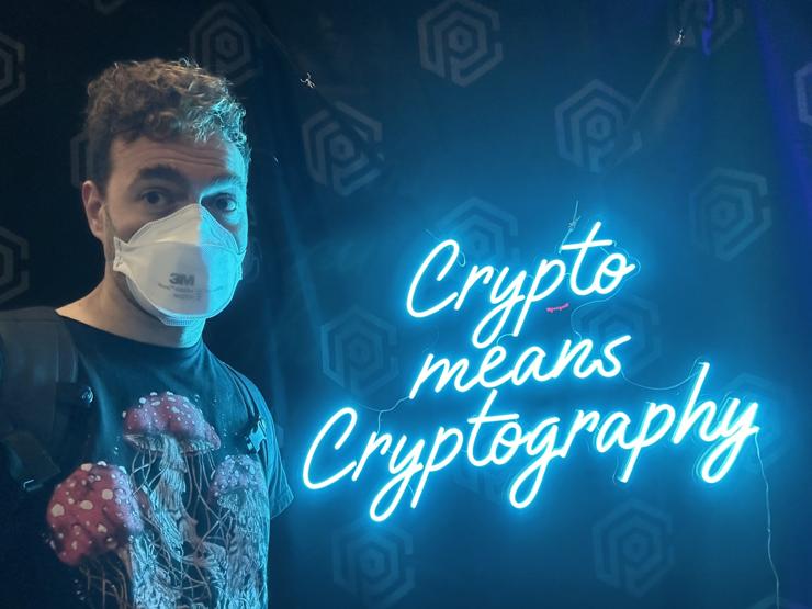 Me standing next to a neon sign that says “Crypto means Cryptography”