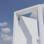 A door frame and partially open door in front of a blue sky with clouds.