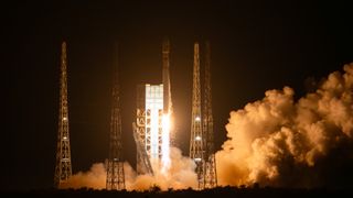 a white rocket lifts off at night above a plume of fire and smoke