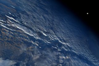 Good morning from the International Space Station! NASA astronaut Nick Hague tweeted this photo of a nearly-full moon setting behind the Earth as a fluffy sheet of clouds covers the land below. A few snow-capped mountains can be seen through a break in the clouds to the bottom right of the image. (Hague did not specify which mountain range is in the photo.)