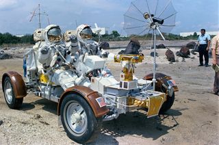 Two astronauts in full spacesuits sit in the LRV trainer buggy at the Kennedy Space Center.