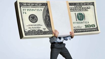 A man in office attire is weighed down by a stack of $100 bills.