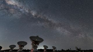 several large antenna dishes point upward under a starry sky