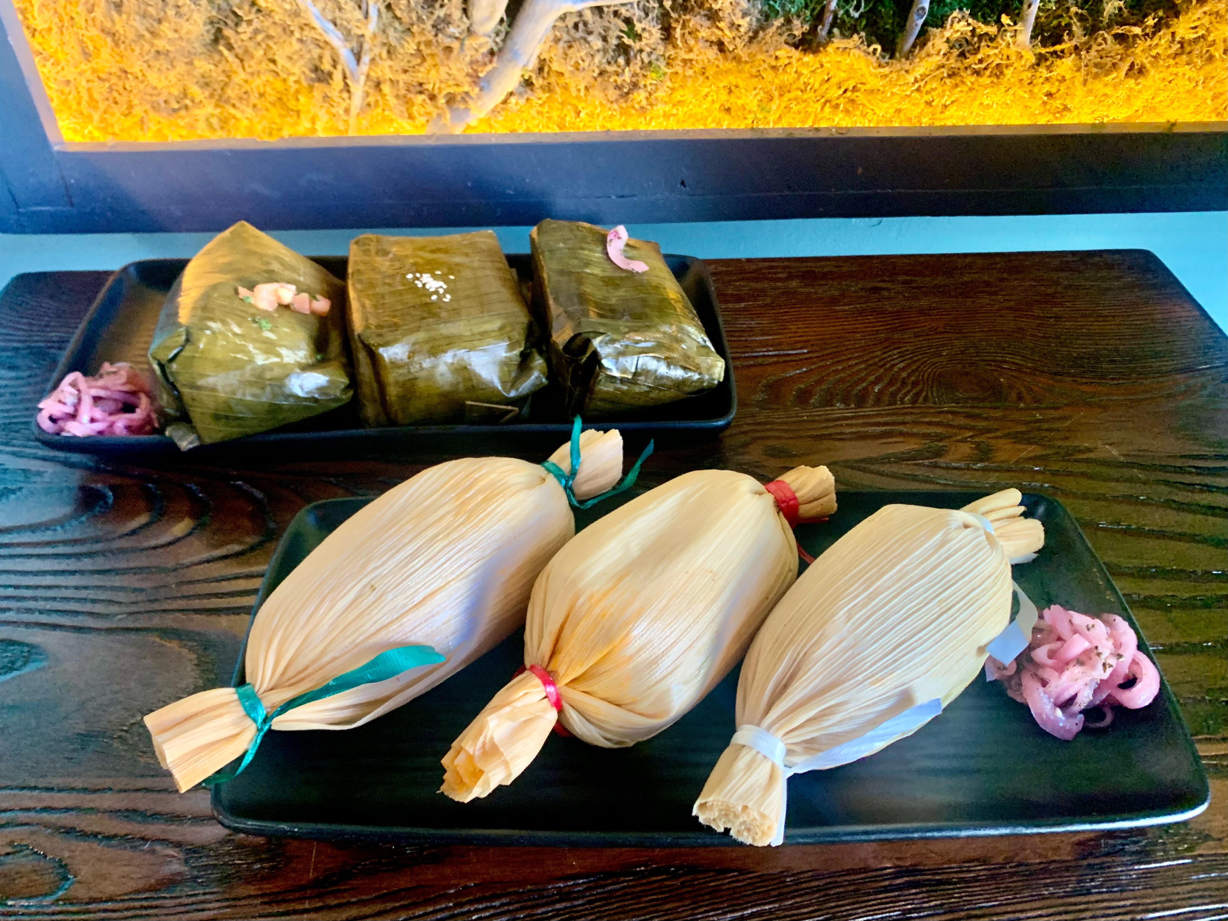 Row of wrapped tamales with colorful twine tied to each end sitting on a wooden table.