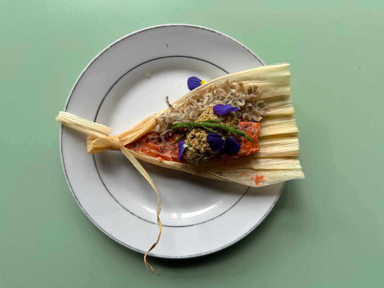 Salmon and wild rice served in a cornhusk and garnished with flowers.