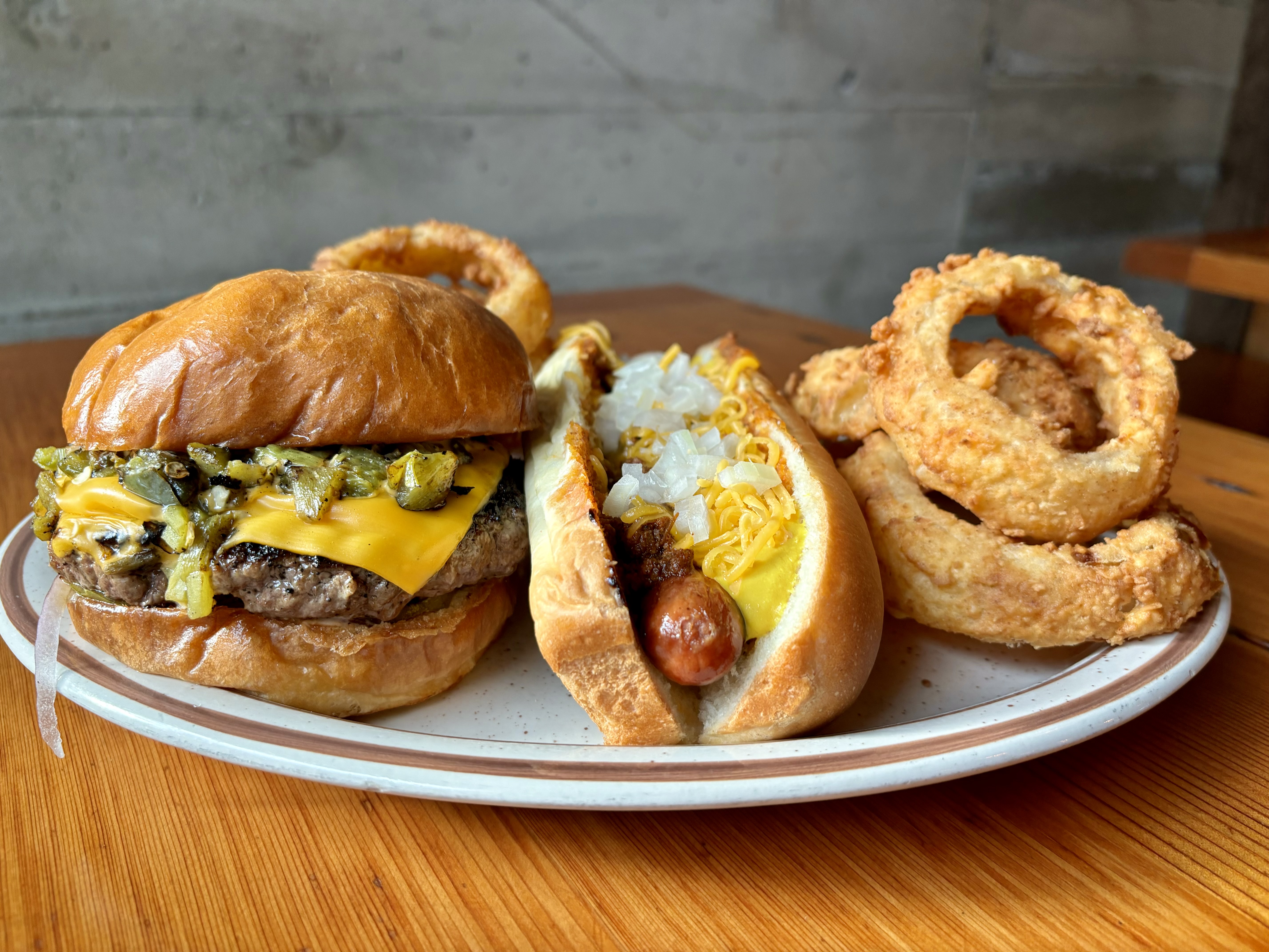 A green chile cheeseburger, hot dog, and onion rings sit on a white plate