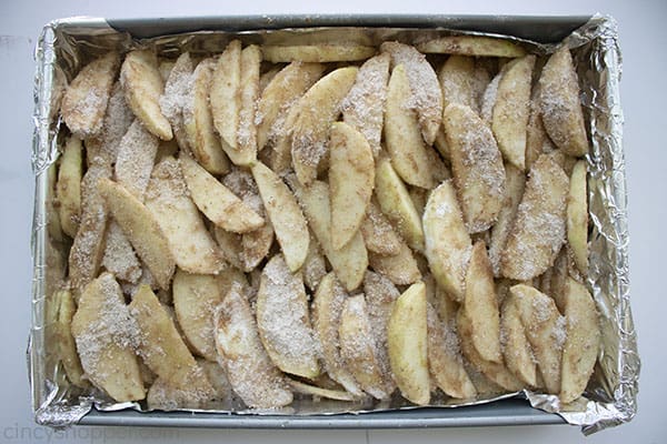 coated apple slices in a rectangular pan lined with foil, evenly spread out 