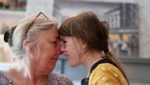 A woman and a girl press their faces together and rub noses.