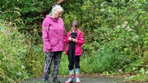 A woman and a girl outdoors looking at their mobile devices.