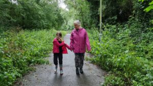 A woman and a girl on a cycleway, holding hands, between trees and weeds.