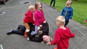 Becky lies on the floor, surrounded by/covered in children.